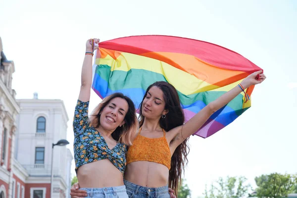 Giovane coppia lesbica sorridente e in possesso di una bandiera arcobaleno. — Foto Stock