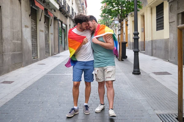 Gay coppia avvolto in un LGBT bandiera abbraccio e sorridente. — Foto Stock