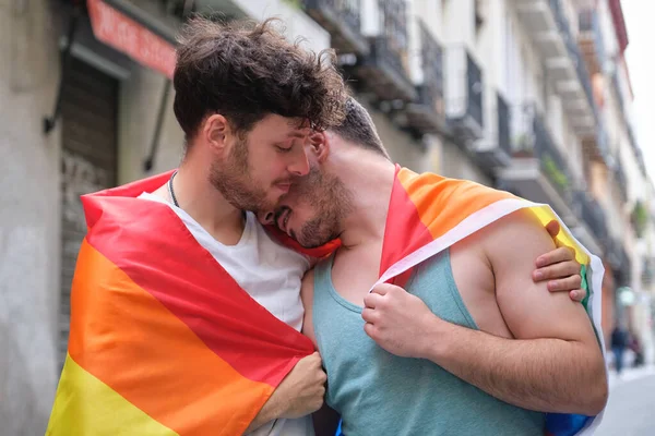 Gay casal envolto no um LGBT bandeira abraçando e sorrindo. — Fotografia de Stock