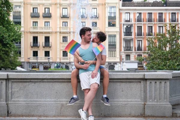 Meleg pár, akik csókolózni készülnek, miközben ölelkeznek az utcán, egy betűtípus mellett ülve.. — Stock Fotó