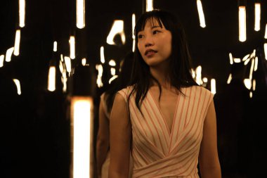 Genç Asyalı kadın poz verir ve kameraya bakar ışık ve aynalarla dolu bir odada..