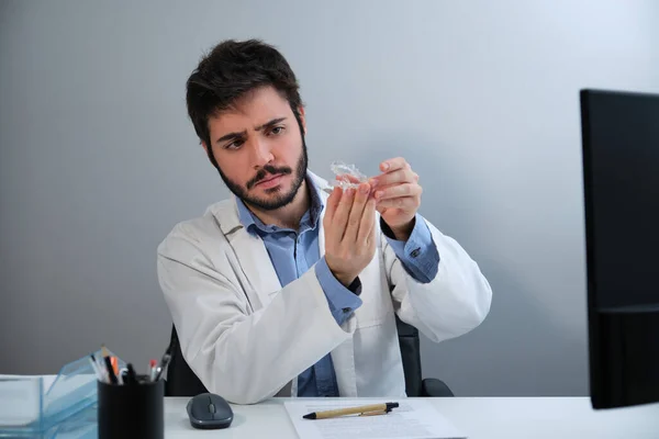 Masada oturan görünmez diş hizalayıcıları tutan genç ortodontist.. — Stok fotoğraf