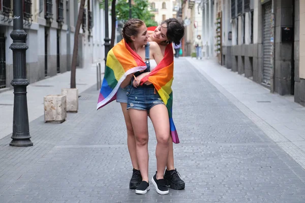 Két nő mosolyog és egymásra tekint egy lgbt zászlóra csomagolva.. — Stock Fotó