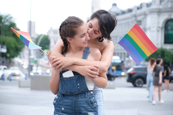 Coppia lesbica che abbraccia, sorride e bacia sulla guancia con bandiere lgbt. — Foto Stock