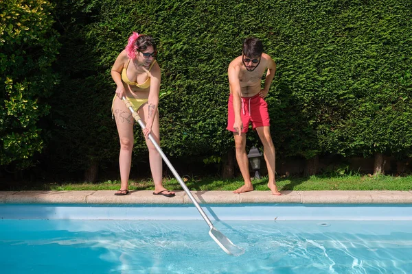 Young couple cleaning swimming pool of fall leaves with cleaning net.