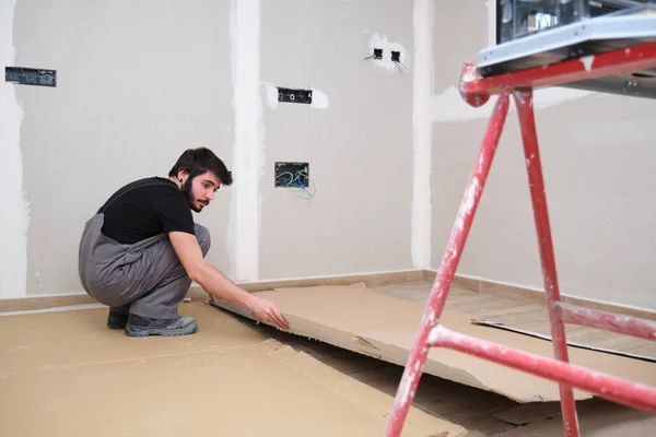 Pintor usando papelão para cobrir o chão de madeira antes de pintar a sala. — Fotografia de Stock