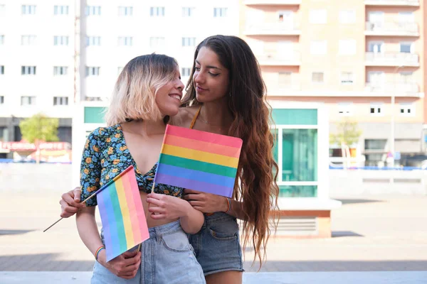 Giovane coppia lesbica guardando l'un l'altro, sorridendo e tenendo bandiere arcobaleno. — Foto Stock
