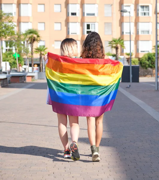 Giovane lesbica camminare avvolto in una bandiera arcobaleno all'indietro. — Foto Stock