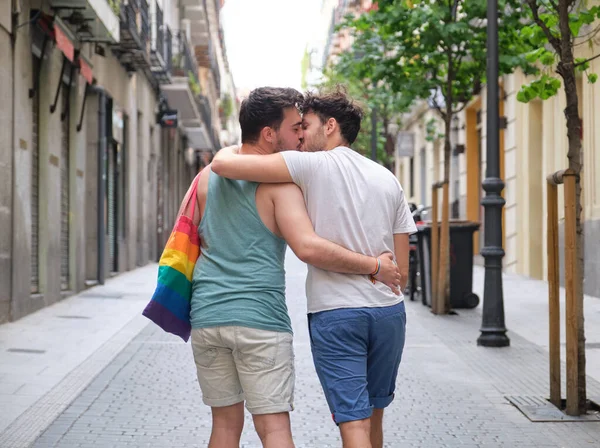 Gay coppia ridere e abbracciare seduta su un panchina tenendo LGBT bandiere. — Foto Stock