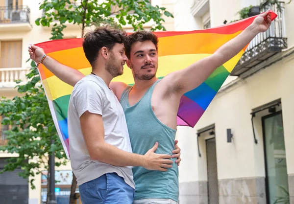Pareja gay sonriendo y abrazándose con una bandera LGBT. — Foto de Stock