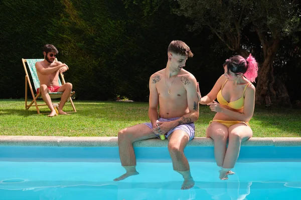 Tre giovani amici caucasici che applicano la protezione solare seduti sul bordo della piscina. — Foto Stock