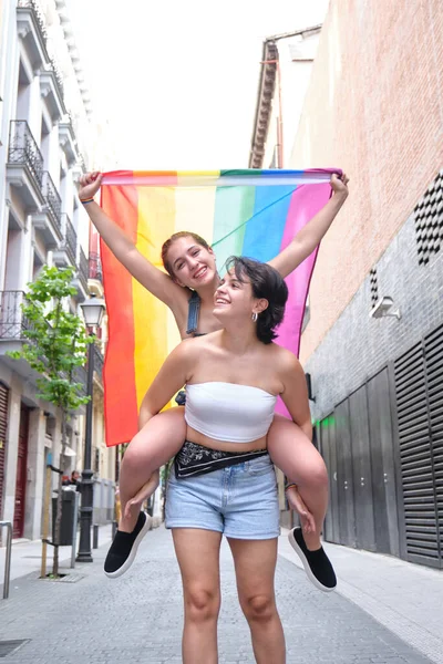 Due ragazze cavalcando con una bandiera lgbt, sorridente. — Foto Stock
