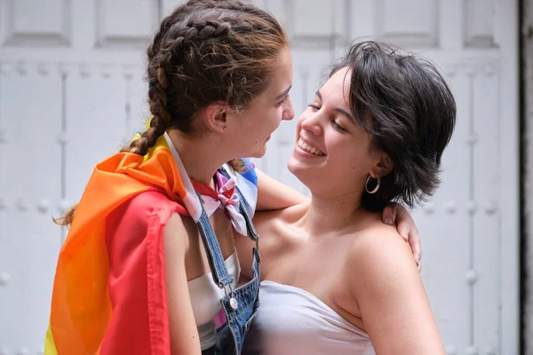 Lesbiche coppia abbraccio, sorriso e guardare l'un l'altro con lgbt bandiera legato come un mantello. — Foto Stock