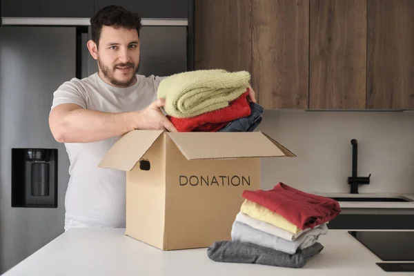 Giovane uomo latino che riempie la scatola delle donazioni di vestiti. — Foto Stock