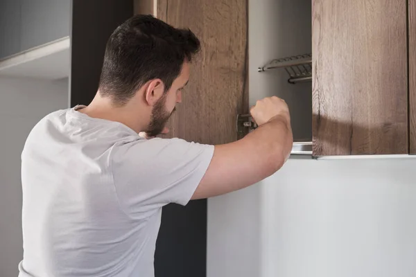 Hombre latino joven instalando armario en la cocina usando un destornillador. —  Fotos de Stock