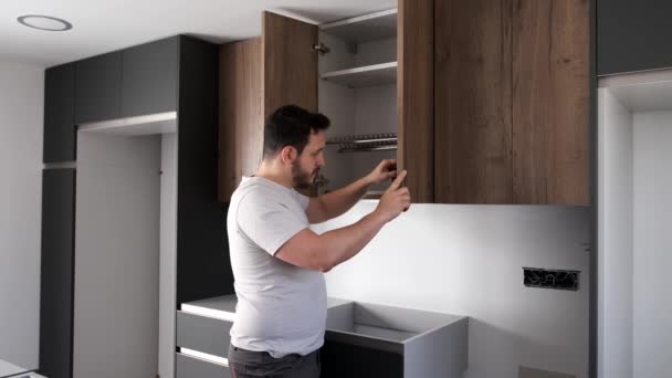Молодий латинський чоловік встановлює шафу на кухні за допомогою викрутки . — стокове відео