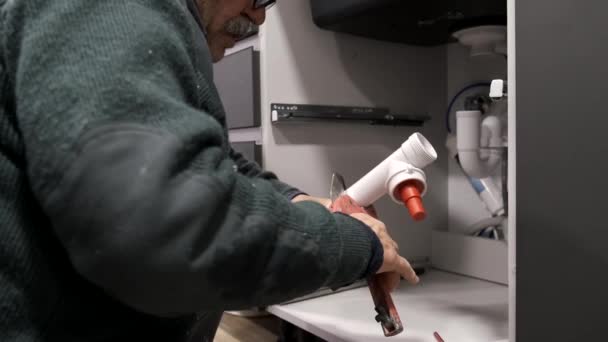 Volwassen loodgieter snijden van de pijp te installeren spoelbak sifon in de keuken. — Stockvideo