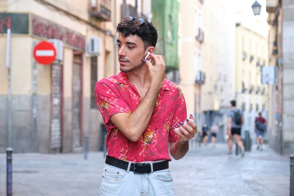 Uzun takma tırnaklı beyaz bir adam kablosuz kulaklıklarını takıyor..