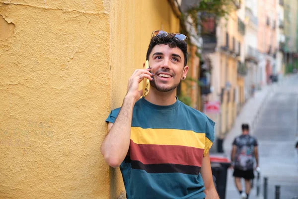 Uzun takma tırnaklı, gülümseyen ve telefonla konuşan beyaz bir genç..