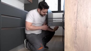 Genç İspanyol bir adam yeni modern bir mutfakta çekmece boyunu ayarlıyor..