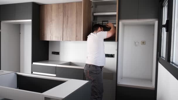 Giovane uomo latino che installa un armadio da cucina accessibile in cucina. — Video Stock