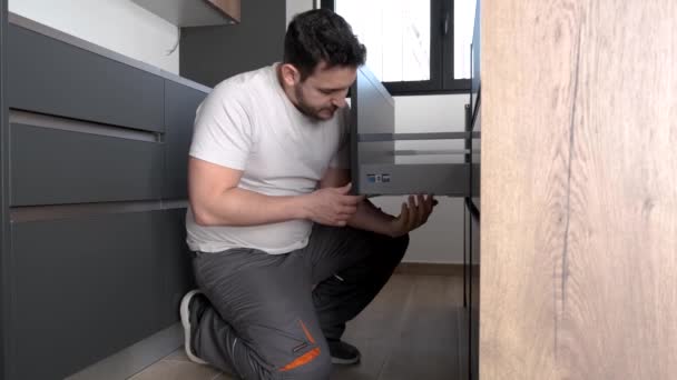 Νεαρός Ισπανός προσαρμόζει το ύψος ενός συρταριού σε μια νέα μοντέρνα κουζίνα.. — Αρχείο Βίντεο