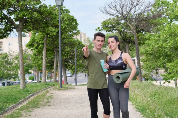 Genç spor çifti parkta dikilirken bir şeye ya da bir yere bakıyor. Fitness konsepti.