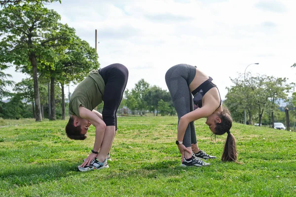 Genç ve sportif bir çift çimlerin üzerinde tüm vücudu esnetiyorlar. Elden ayağa yoga pozu.
