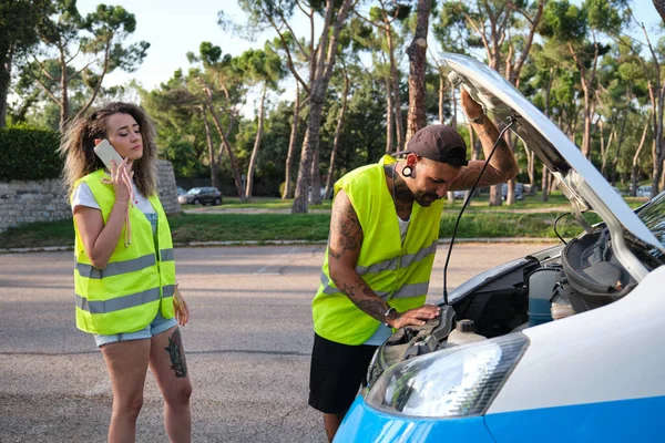 Mladý tetovaný pár v reflexní bezpečnostní vestě volající po silniční pomoci. — Stock fotografie