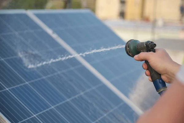 Tecnico irriconoscibile che pulisce pannelli solari con un tubo. — Foto Stock