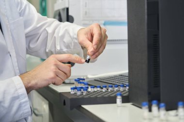 Laboratuvar önlüklü bilim adamı numuneyle birlikte HPLC sisteminin otomatik amplifikatörüne örnek koyuyor..