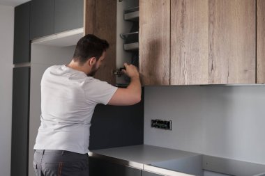 Genç Arjantinli adam tornavida kullanarak mutfağa dolap kuruyor. Modern mutfak mobilyalarının montajı.