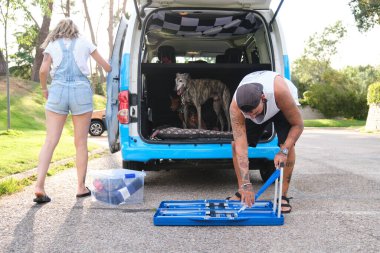 Genç dövmeli çift, köpekleriyle minibüsün yanında piknik masasını bir araya getiriyorlar..