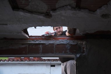 Genç adam tokmak kullanarak evin tavanını aşağı çekiyor..