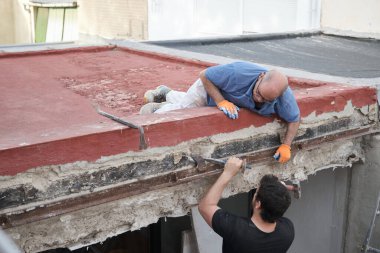 İnşaat evindeki eski metal kirişleri çekiç ve keskiyle söken iki duvar ustası..