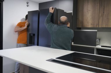 İki teknisyen yeni bir modern mutfağa Amerikan buzdolabı kuruyor..