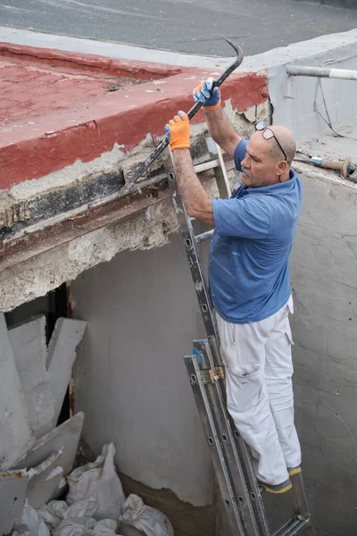 Olgun duvar ustası inşaat evindeki eski metal kirişleri levye kullanarak kaldırıyor..