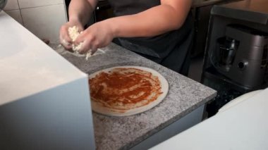 Lokanta mutfağında çiğ pizzaya peynir ekleyen erkek ellerine yakın çekim. Pizzacı..