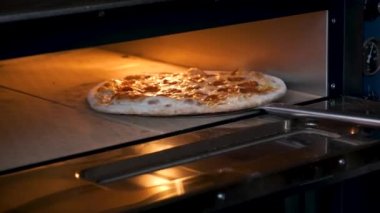 Putting pepperoni pizza into the oven in a restaurant kitchen. Pizzeria.