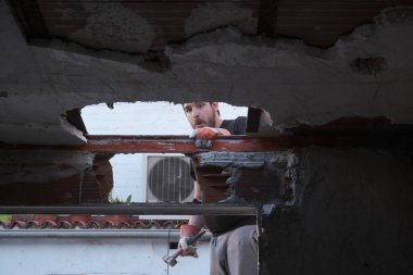 Genç bir adam tokmak kullanarak evin tavanını yıkıyor ve başka bir şeyi daha kırdığını fark ediyor..