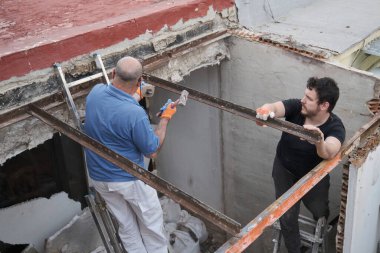 İnşaat evinde eski metal kirişleri söken iki duvar ustası..