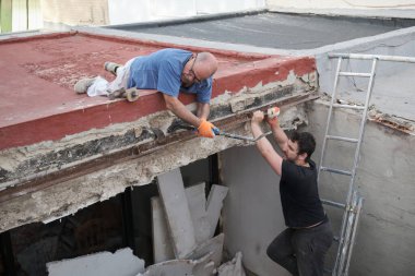 İnşaat evindeki eski metal kirişleri çekiç ve keskiyle söken iki tamirci..