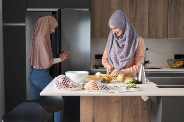 İki Müslüman kadın buzdolabını açıyor ve modern mutfakta salata hazırlıyorlar..