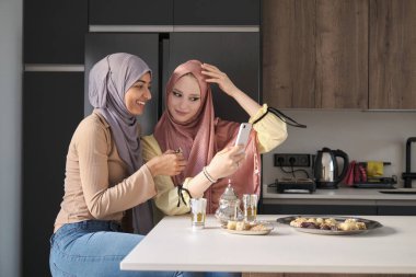 Mutfak masasında çay ve Arap tatlısı içerken akıllı telefon kullanan iki Müslüman kadın..