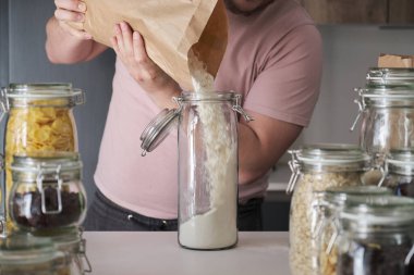 Unrecognizable latin man filling up a jar with wheat flour from a paper bag. Food in bulk delivery.
