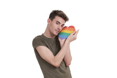 Young caucasian man smiling at camera with lgbt flag heart, isolated on white background.