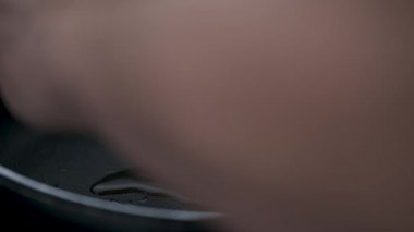 Male hand cooking and adding salt to egg in olive oil in frying pan.