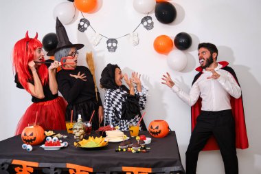 Man dressed as vampire scaring people at a costume Halloween party in a house.