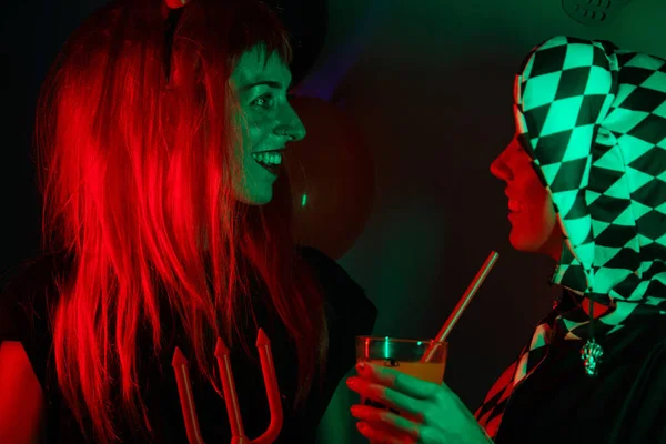 Two women dressed as a harlequin and devil at a costume Halloween party.