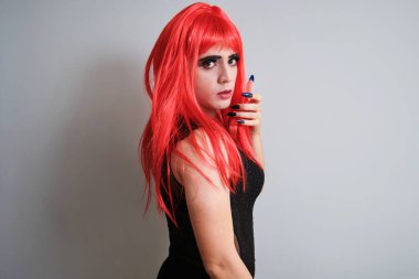 Kırmızı peruk takan ve gri arka planda kameraya bakan travesti portresi. LGBTQ eşcinseli.